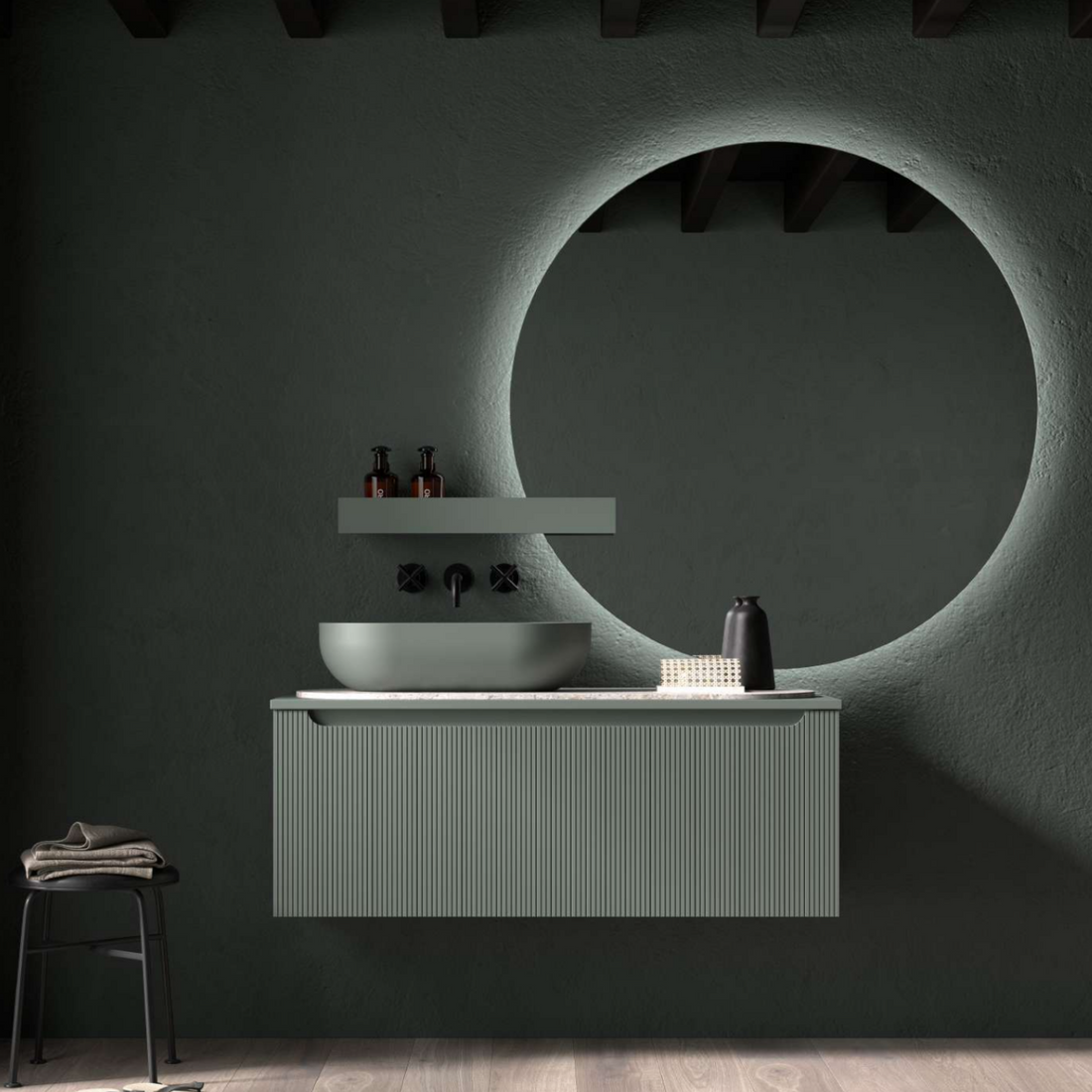 Baño con mueble suspendido Kimono verde, lavabo blanco, grifería oscura y espejo redondo retroiluminado.